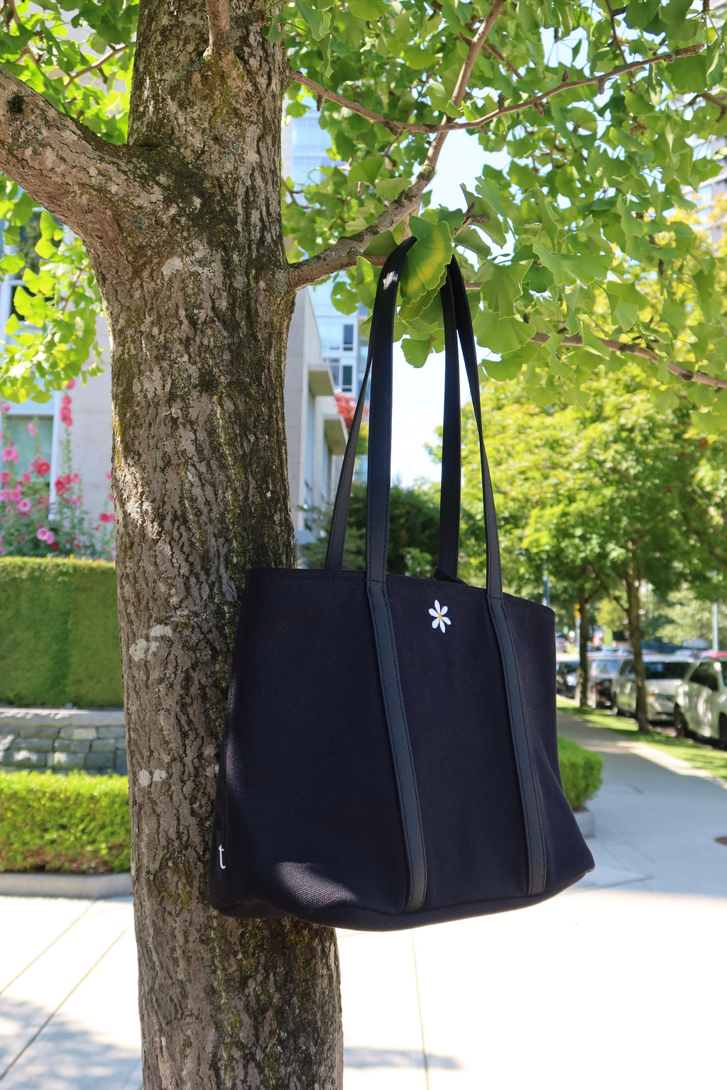 Black tote bag hanging on a tree branch with a cityscape in the background