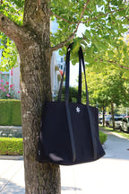 Black tote bag hanging on a tree branch with a cityscape in the background