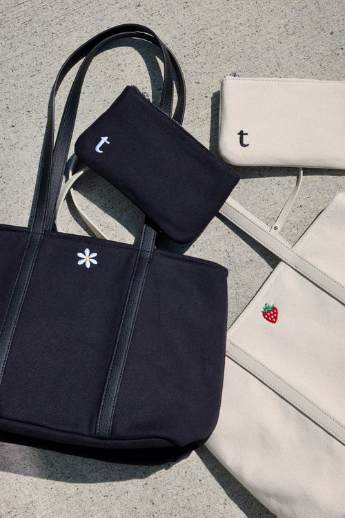 A black tote bag with flower embroidery and a white tote bag with a strawberry embroidery. minimalist canvas made tote bags for everyday use