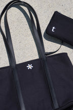 Black tote bag with a white flower design and matching pouch on a concrete surface. includes a small pouch that has interior credit card holder, and interior pockets. small flower embroidery, canvas tote bag