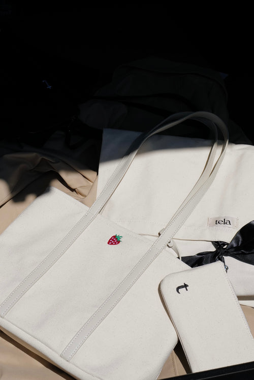White bag with strawberry embroidery and visible brand name on a dark background